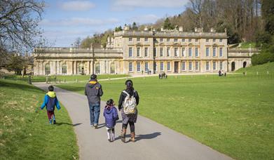 A family walking through the parkland in front of the house at Dyrham Park, participating in the trail. 
