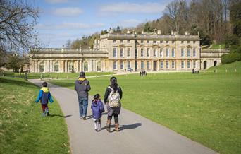A family walking through the parkland in front of the house at Dyrham Park, participating in the trail.