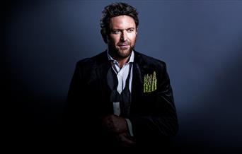 Portrait image of celebrity chef James Martin, wearing a black suit which a handful of asparagus in his jacket pocket.