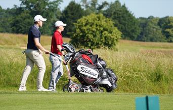 Two golfers walking to a hole on a course with their kit