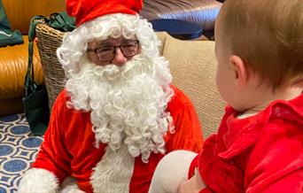 A man dressed as Father Christmas talking to a child