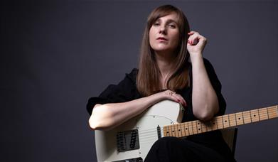 A woman posing with a guitar on her lap
