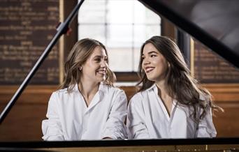 Two women sitting at the piano facing each other and smiling