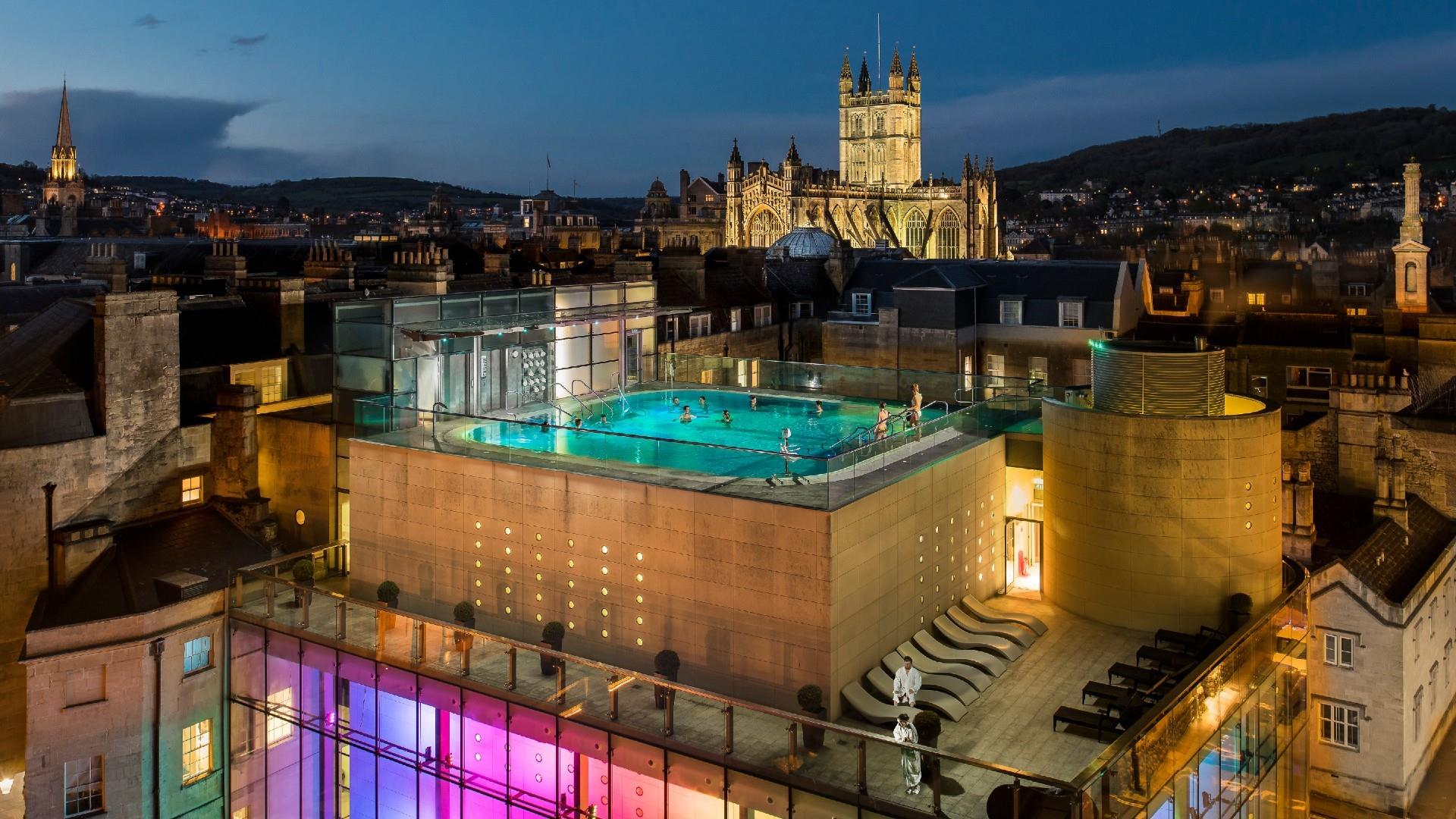 An image of the Thermae Bath Spa rooftop pool and Bath's city skyline at night.
